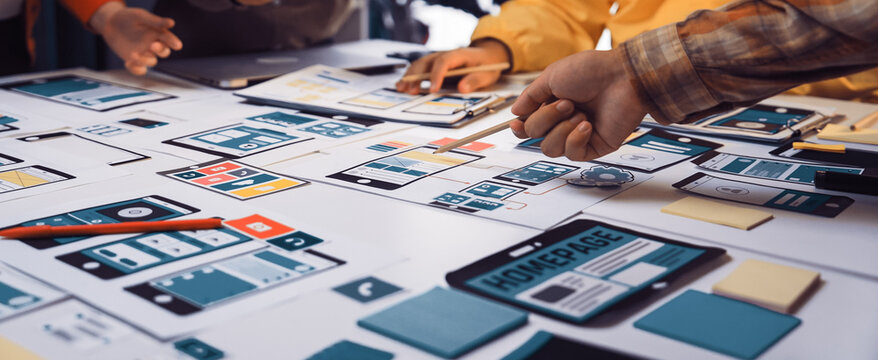 A diverse team engages in a productive brainstorming session, developing mobile app wireframes and design concepts on a bright, organized workspace table. SACTR - Powered by Adobe