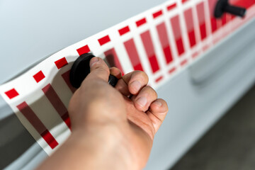 Hand of worker installing vinyl film stickers. Gluing speed stripes from red sticker on the side of the car.