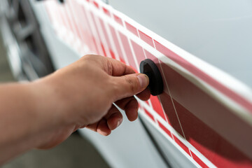 Hand of worker installing vinyl film stickers. Gluing speed stripes from red sticker on the side of the car.