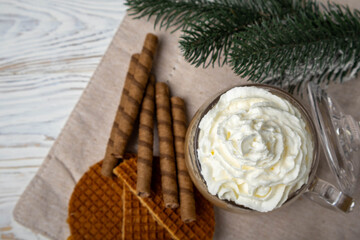 Hot coffee with whipped cream among cookies, pine branches, and festive Christmas spirit. A concept for greeting cards.