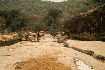 Rear view of a female tourist having fun on a dry river bed amidst acacia shrub forest in Ngurunit District, Marsabit County, Kenya 