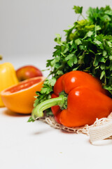 Various fresh vegetables falling out of a string bag on a white background