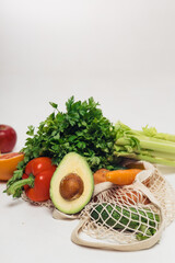Various fresh vegetables falling out of a string bag on a white background