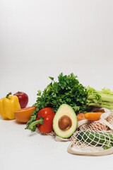 Various fresh vegetables falling out of a string bag on a white background