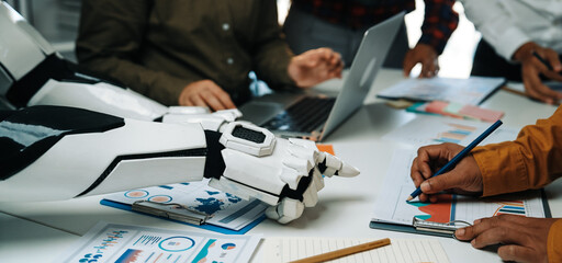 In a modern office setting, a robot arm collaborates with human participants during a meeting to analyze data, featuring charts and documents that showcase innovative strategies.Noogenesis
