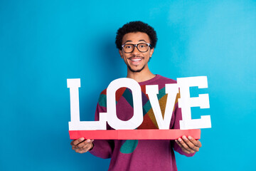 Young man holding a decorative love sign, smiling confidently against a vibrant blue background