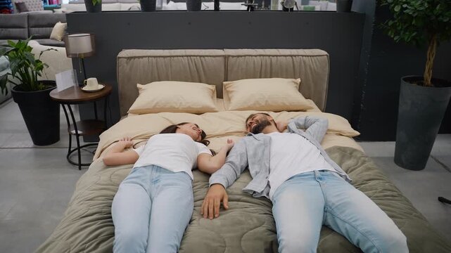 Newlyweds couple testing a new bed mattress in a furniture store