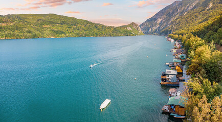 Drina river canyon with houseboats and a boat creating trails of white wake on blue water along forested mountains