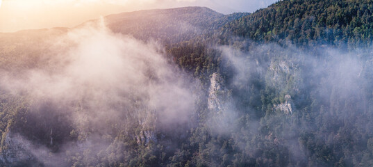 Lush green mountains and dense forest rising through morning fog and clouds during a beautiful sunrise vista
