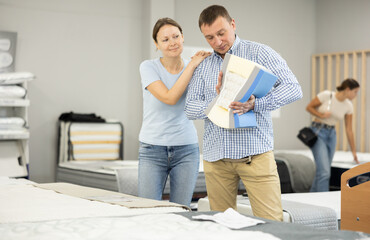 Couple study cross section structure of spring mattress in furniture store. They tests durability...