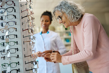 Happy senior woman choosing eyeglasses in drugstore.