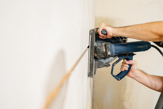 Worker cutting a straight groove in a plaster wall with an electric wall chaser tool to install electrical cables during interior renovation and remodeling project, concept of home improvement.