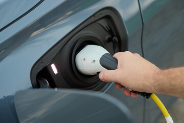 A person connects a charging cable to the electric vehicle at a public charging station in a busy urban environment. The setting emphasizes a commitment to eco-friendly transportation.