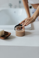 Woman Get Cosmetic Body Scrub From Jar Sitting On Bath In Bathroom