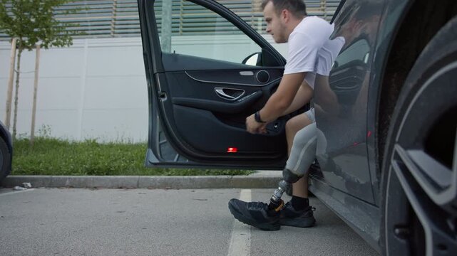 Driver, a young man with a prosthetic leg, getting out of a parked car and moving away towards the building, close up shot. Mobility and independence concept.