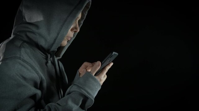 Lady developing program in laptop in dark. A view of lady in hoody making an internet program on her phone on the black background
