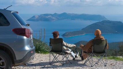 Tourists couple relaxing in camping chairs enjoying scenic seascape view. Carefree tourists sitting in camping chairs, savoring panoramic seascape while parked near vehicle on scenic mountain overlook - Powered by Adobe