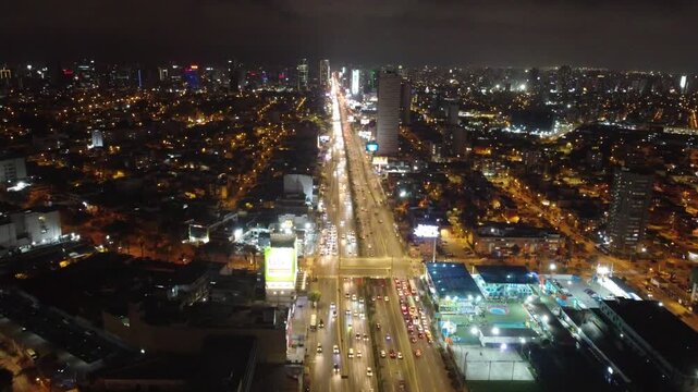 Aerial view of a brightly illuminated highway with heavy traffic flowing through a dense city at