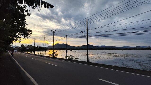 Sunset over rural road with mountain reflection in flooded field - Powered by Adobe