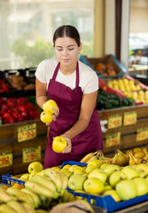 Smiling girl seller is showing assortment of fresh apples in vegetable shop