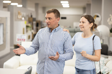 Fototapeta premium Interested man and woman strolling together through furniture showroom, curiously looking at various pieces for home and discussing choice