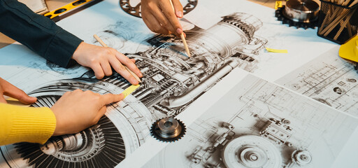 Engineers collaborate over detailed blueprints of an aircraft engine. The scene captures hands pointing to specific components, showcasing teamwork and innovation in design. SACTR