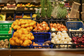 Fresh vegetables displayed in supermarket crates including potatoes, onions, and herbs. Concept of healthy organic food and grocery shopping