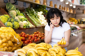 Young girl choosing fresh yellow bananas in fruit and vegetable section of supermarket