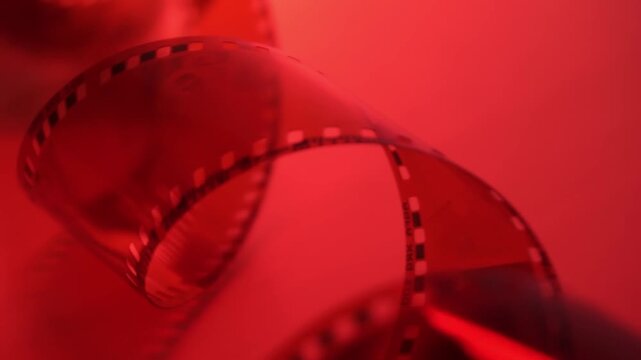 35mm negative photographic film in rotation in red room, camera darkroom. Slightly rolled film strip isolated on red background. Analog film strips. Analog photography. Close-up