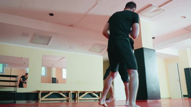 Karate practitioners sparring inside dojo on red mat, wearing protective gloves, engaged in close range combat training, showing focus, movement, reaction, balance, and determination during practice