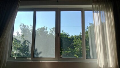The bright sunlight shines through a window, revealing a vibrant blue sky and lush green trees outside on a beautiful, sunny day.