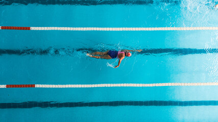 Aerial top view of a swimmer in a blue pool performing freestyle stroke between lane dividers. The...