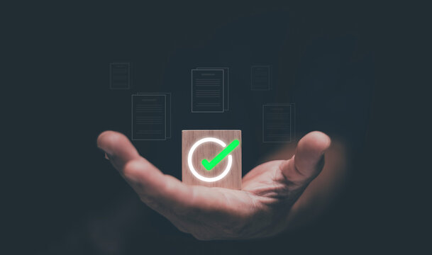 Business approval and verification concept. Glowing green check mark icon on wooden block on hand, symbolizing quality assurance, successful validation, compliance and trusted digital confirmation.