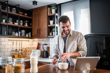 Young man preparing healthy breakfast while watching tablet
