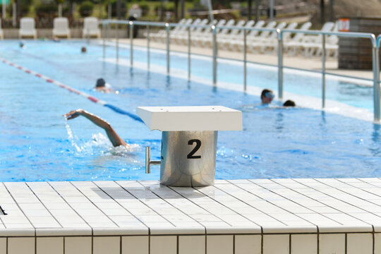 The starting blocks ready to jump into the pool and the swimmers are swimming - Powered by Adobe