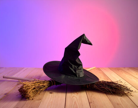 Witch hat and broomstick on a wooden surface with a colorful gradient background for Halloween.