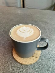 A warm cup of cappuccino with elegant latte art on a gray stone table, captured from above in natural light.
