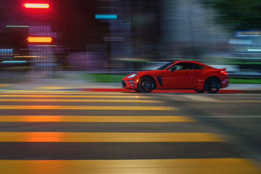 LOS ANGELES, CA - February 02, 2025: Red sports coupe car Toyota GR86 driving through night street intersection. Blurred motion.