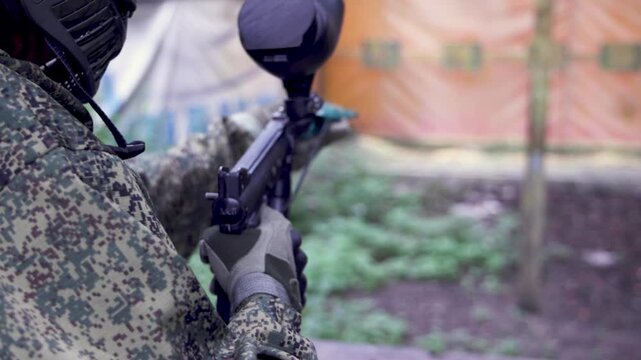 Paintball game, team in camouflage protective uniform with paintball guns and ammunition, strikeball arena battlefield, paintballer aiming and shooting at opponents, airsoft players match tournament