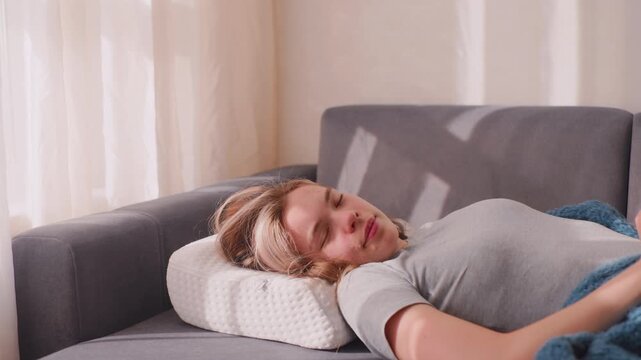 Lady finally wakes up and stretches herself on sofa, resting on white pillow with soft blanket, sunlight casting warm shadows across cozy living room
