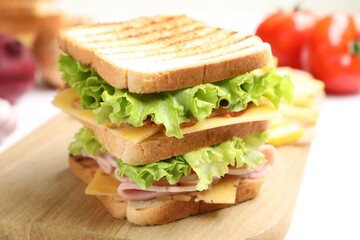 Tasty sandwich with ham, bacon, cheese and vegetables on white table, closeup