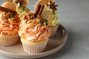 Delicious cupcakes with colorful cream, spices and nuts on grey table, closeup