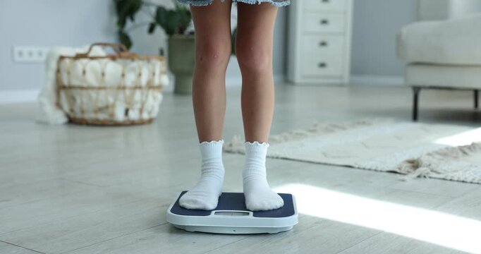Little girl measuring her weight on scales at home, closeup