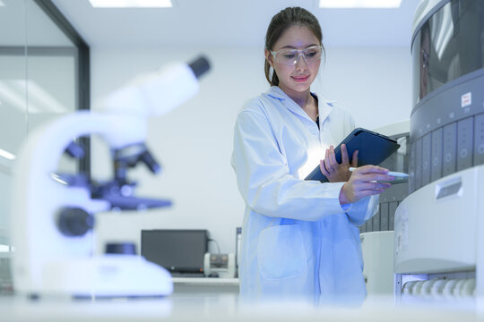 A thoughtful female scientist in a modern lab pauses to contemplate her research, holding a tablet and planning the next steps of an experiment amidst high-tech analytical equipment.
