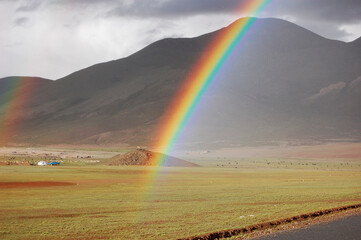 Beautiful rainbow appearing over vast grassland with mountains in the background