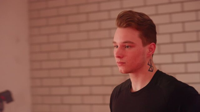 Side view of chap with short hair and neck tattoo jogging against brick wall, wearing black shirt, calm focused expression, representing individuality, strength, personality, and modern urban