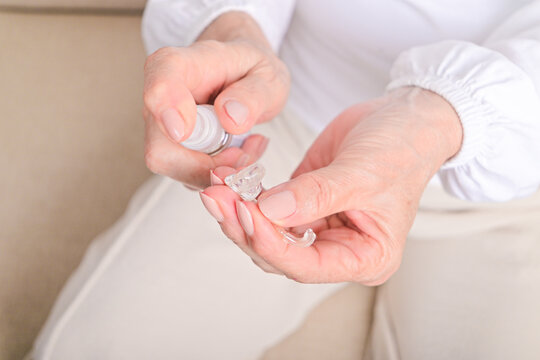 Elderly woman disinfecting hearing aid with cleaning spray, close-up of hands showing hygiene and maintenance of hearing device for senior auditory health care.