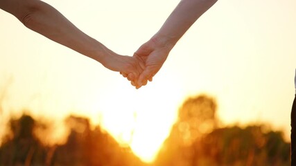 Two silhouetted hands of men and a women against warm sunset. Scene symbolizes love, family, support, unity. The background features a blurred landscape with soft lighting.