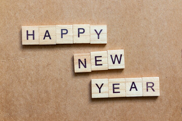 Wooden letter tiles arranged to spell HAPPY NEW YEAR on a brown textured background