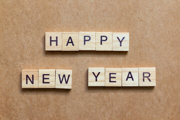 Wooden letter tiles arranged to spell HAPPY NEW YEAR on a brown textured background
